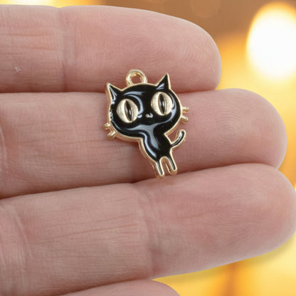Hackberry Creek black enamel cat charm with gold-plated metal alloy held between fingers for jewelry making
