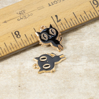 Hackberry Creek black enamel cat charms with gold-plated edges, shown next to a ruler for scale.