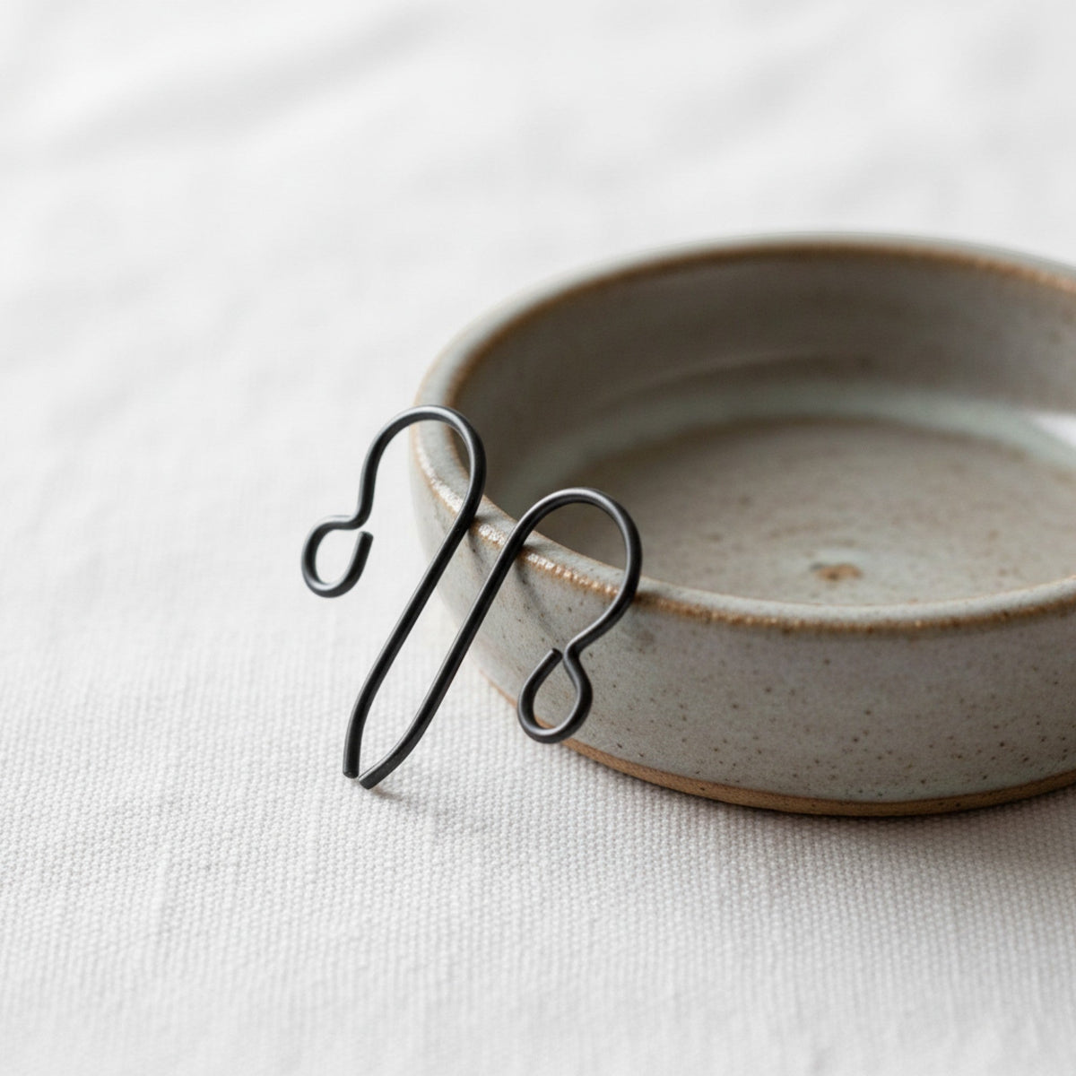 Hackberry Creek hypoallergenic matte black niobium earring hooks resting on a small ceramic dish on linen fabric.