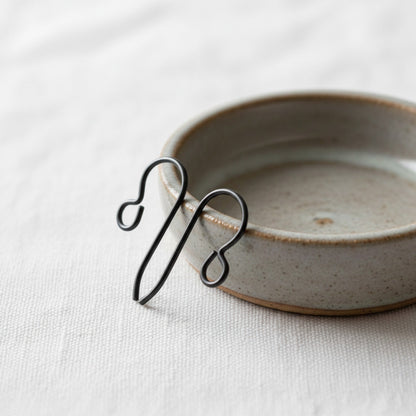 Hackberry Creek hypoallergenic matte black niobium earring hooks resting on a small ceramic dish on linen fabric.