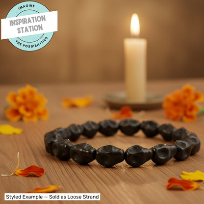 Hackberry Creek black magnesite skull beads arranged in a circle on a wooden table with marigolds and a lit candle.