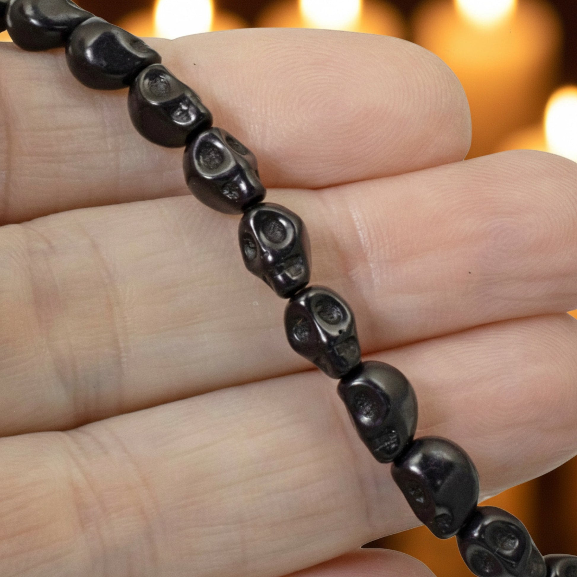 Hackberry Creek black magnesite skull beads on a strand held in a hand for DIY Halloween jewelry making.