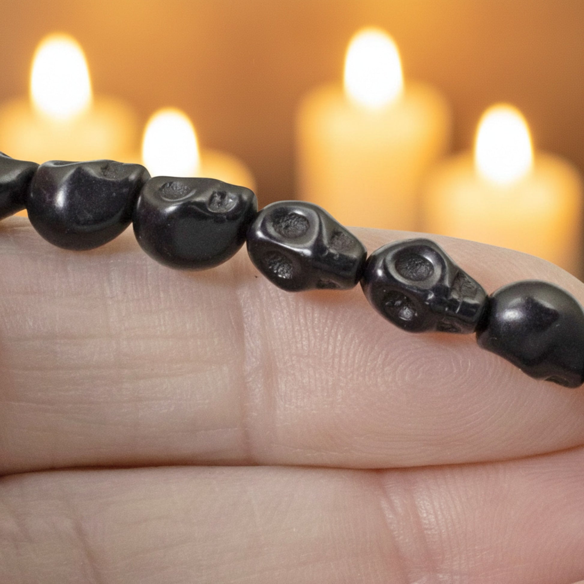 Hackberry Creek black magnesite skull beads on a strand, held in hand with blurred candles in the background.