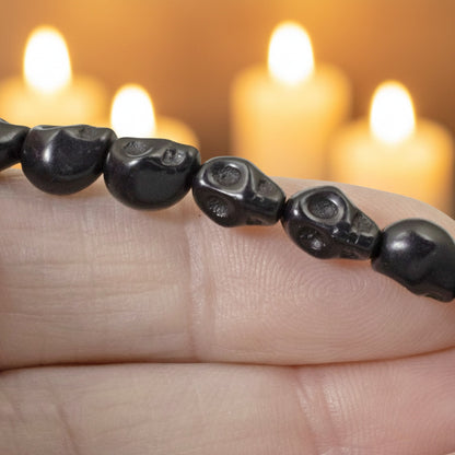 Hackberry Creek black magnesite skull beads on a strand, held in hand with blurred candles in the background.