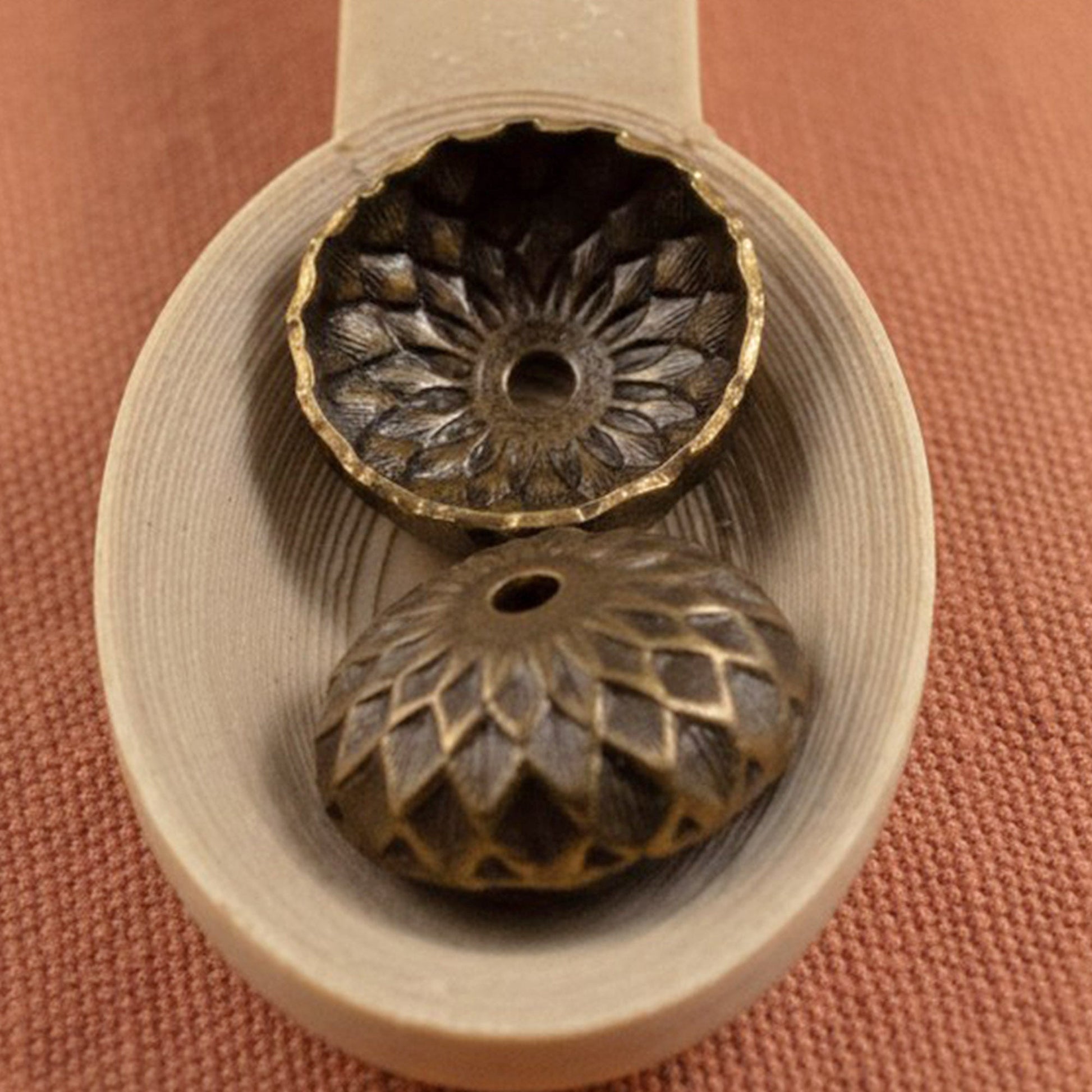 Hackberry Creek 13mm natural brass acorn bead caps with detailed sunflower relief stamping on a wooden spoon