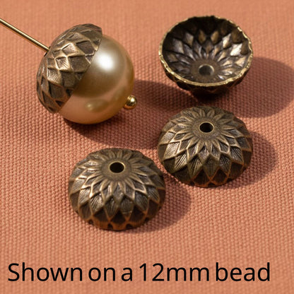 Hackberry Creek 13mm natural brass acorn bead caps with detailed sunflower relief pattern on a textured fabric surface