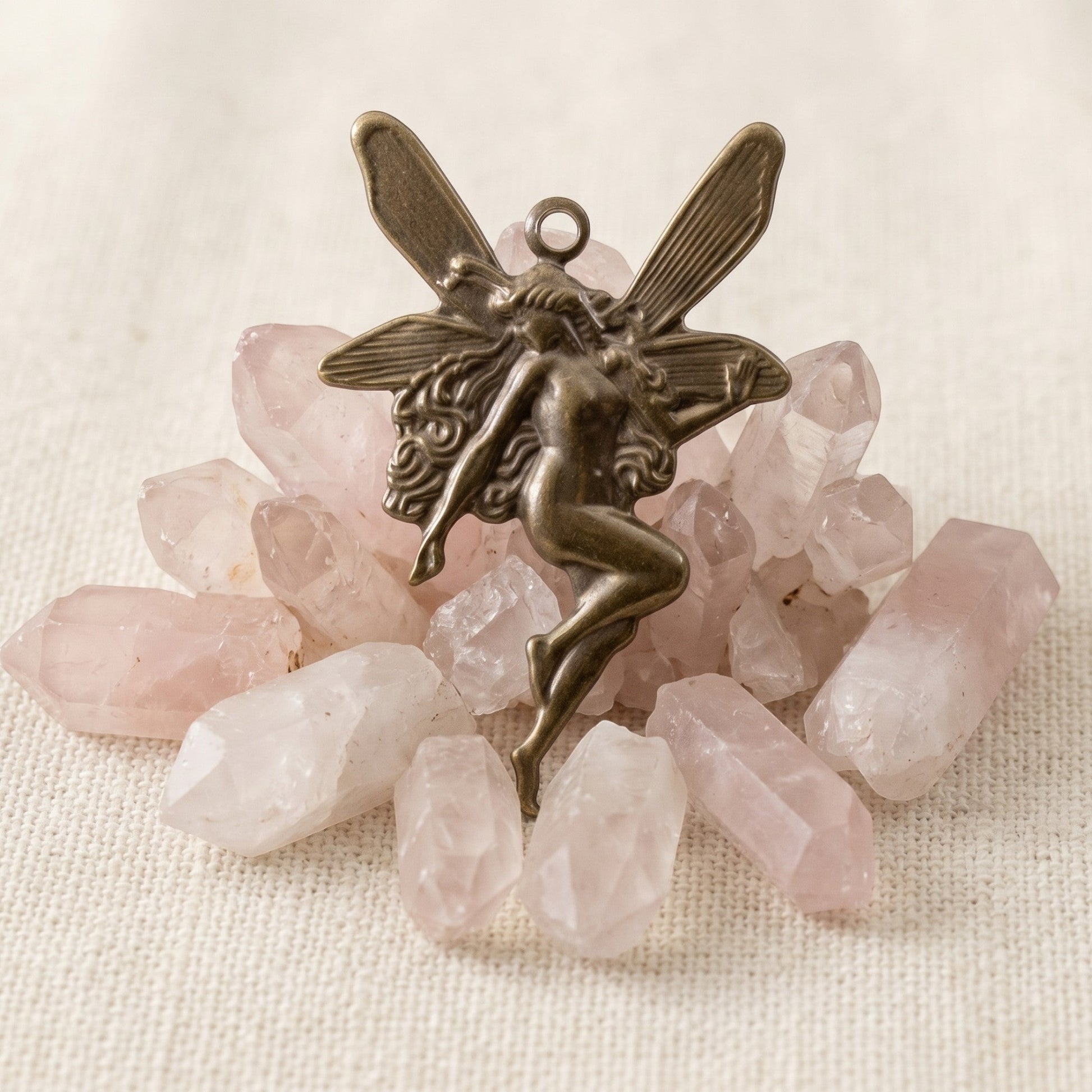 Hackberry Creek antiqued brass Art Nouveau fairy charm resting on a cluster of raw rose quartz crystals.