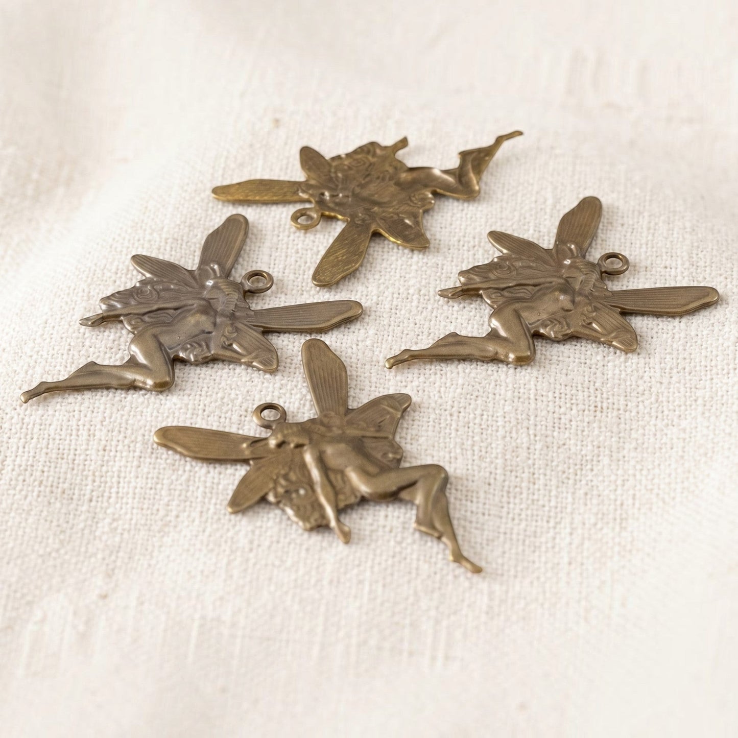 Hackberry Creek set of four antiqued brass Art Nouveau fairy charms with dimensional concave stamping on fabric.