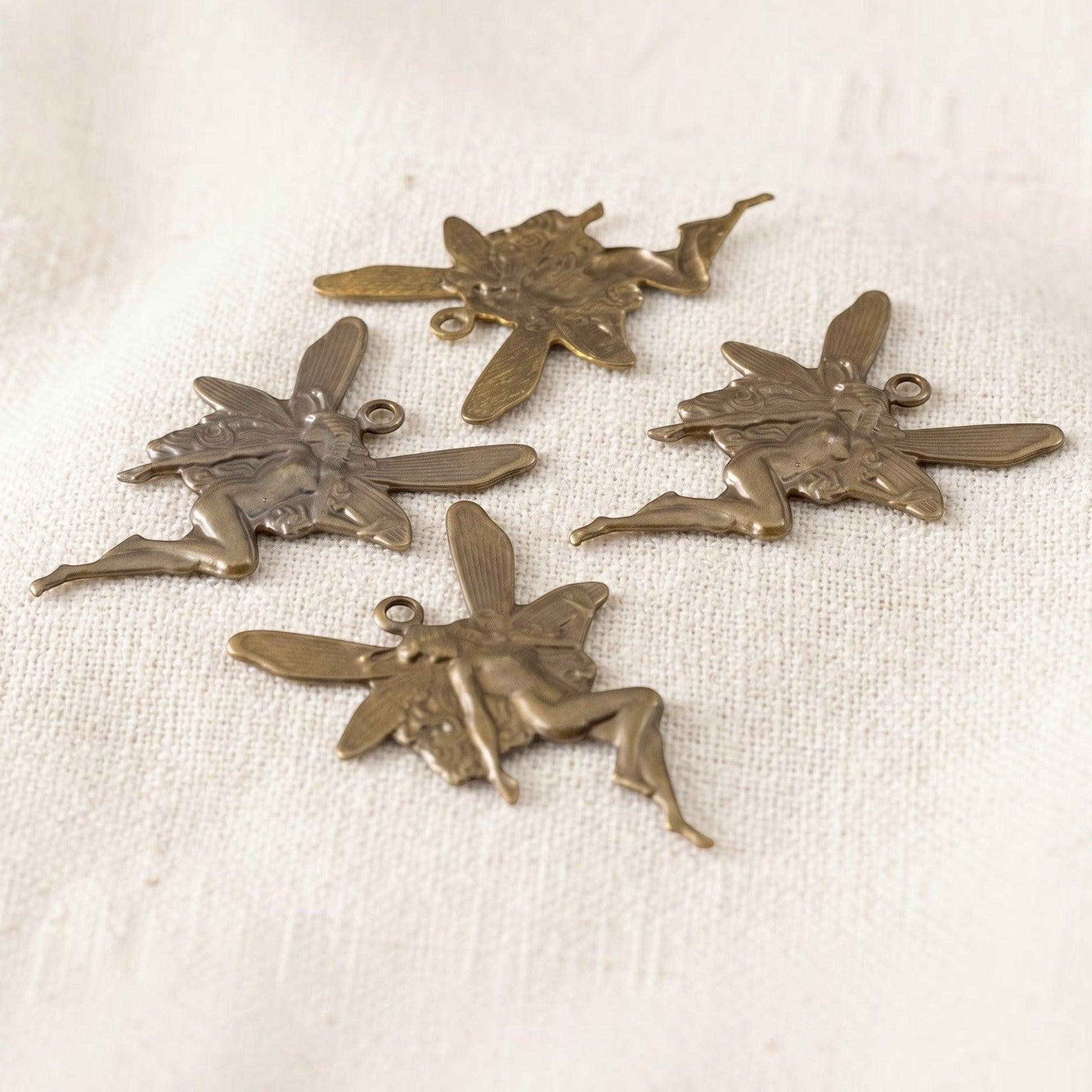 Hackberry Creek set of four antiqued brass Art Nouveau fairy charms with dimensional concave stamping on fabric.