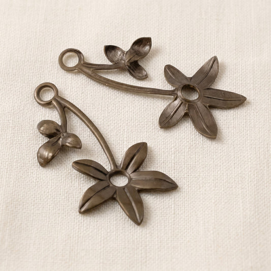 Hackberry Creek antiqued brass violet sprig charms with two holes for jewelry making on a textured fabric background.