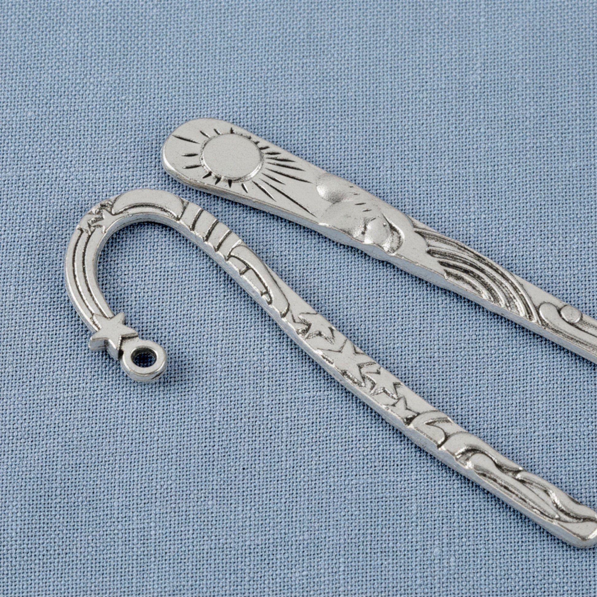 Hackberry Creek antique silver metal bookmarks featuring celestial sun and star designs on a blue fabric background.
