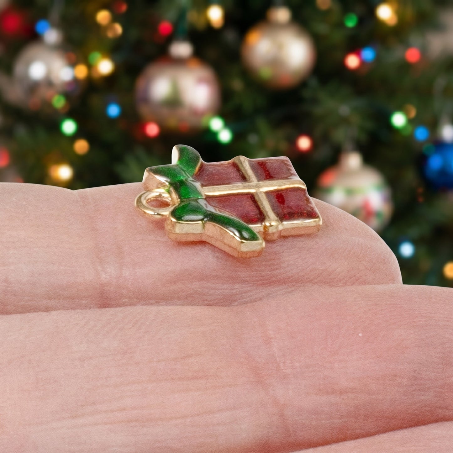 Hackberry Creek Christmas gift charm with red enamel and green bow on a gold metal base held on a finger