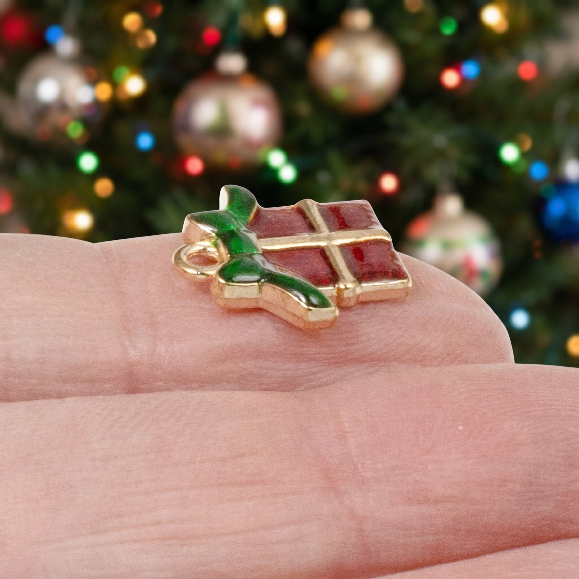 Hackberry Creek Christmas gift charm with red enamel and green bow on a gold metal base held on a finger