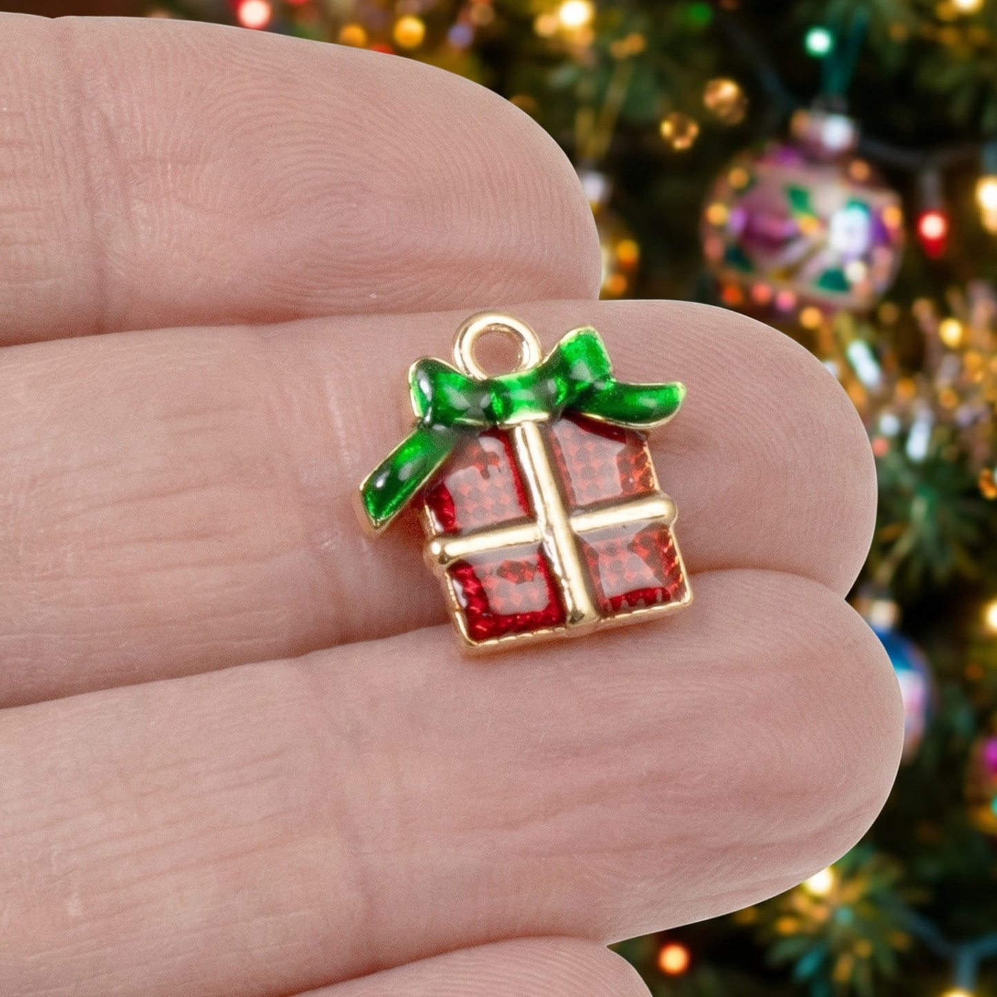 Hackberry Creek Christmas gift charm with red enamel and green bow, held in hand against a blurred holiday tree.