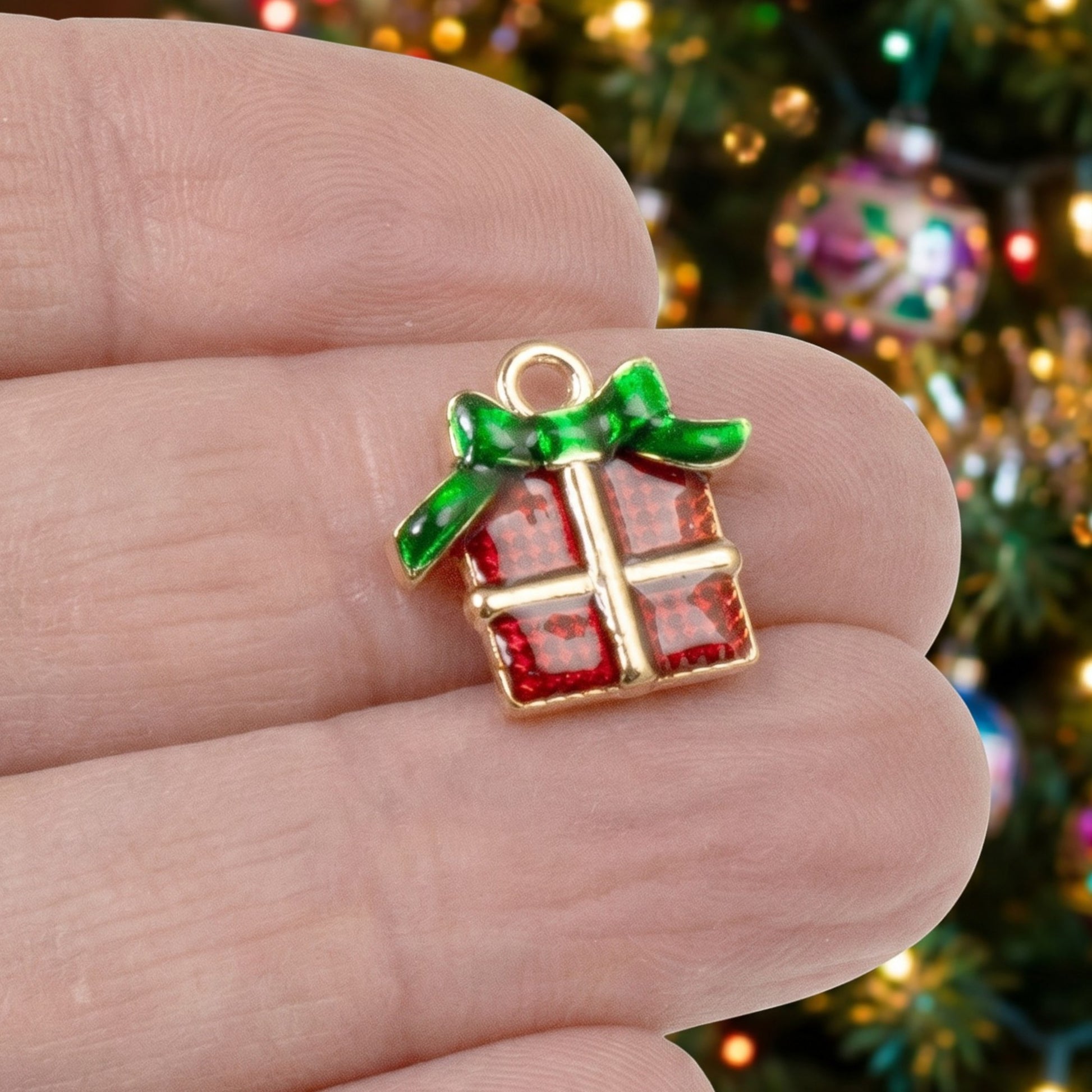Hackberry Creek Christmas gift charm with red enamel and green bow, held in hand against a blurred holiday tree.