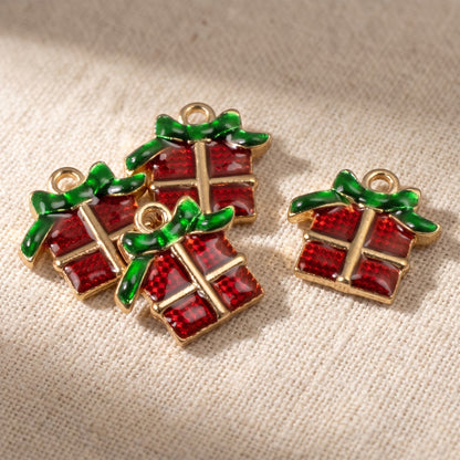 Hackberry Creek Christmas present charms with red enamel gift boxes and green bows on a textured fabric background.