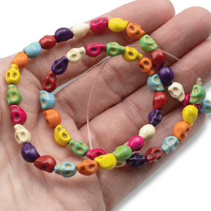 Hackberry Creek colorful magnesite skull beads on a 15-inch strand held in a hand for Halloween jewelry crafts