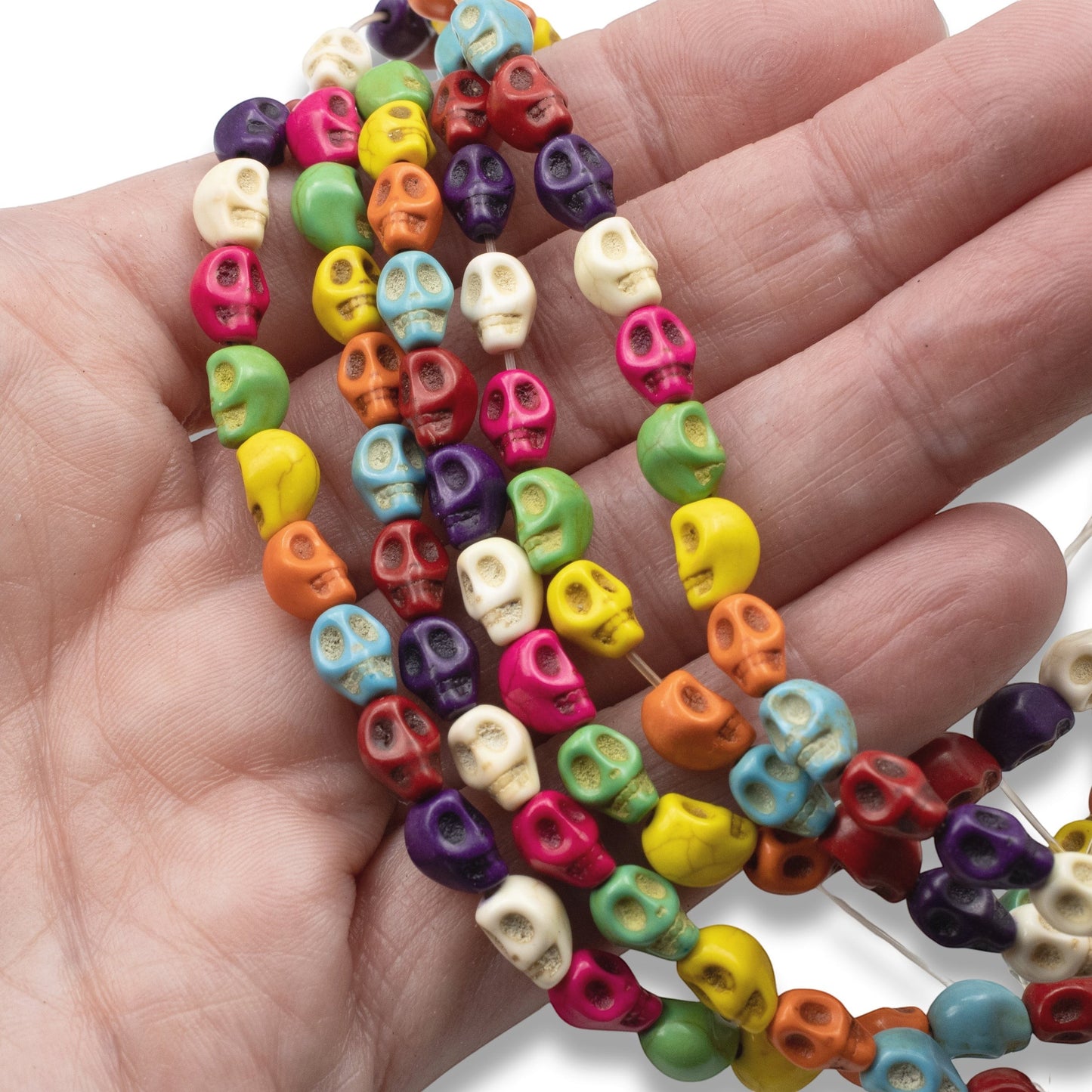 Hackberry Creek colorful magnesite skull beads on a strand held in a hand for Halloween and Day of the Dead jewelry.