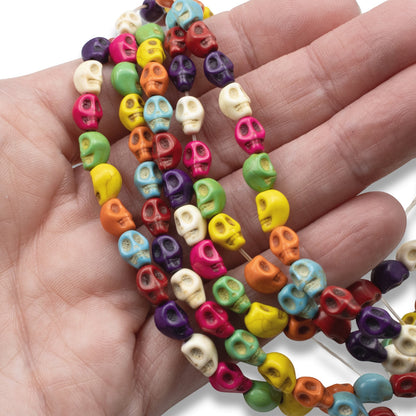 Hackberry Creek colorful magnesite skull beads on a strand held in a hand for Halloween and Day of the Dead jewelry.