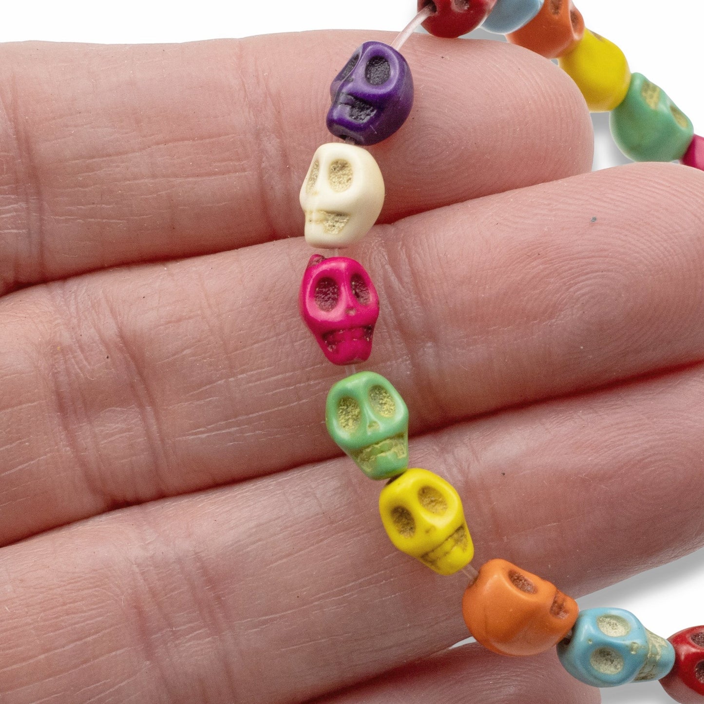 Hackberry Creek colorful mini skull magnesite stone beads on a strand held in a hand for Halloween jewelry crafts.