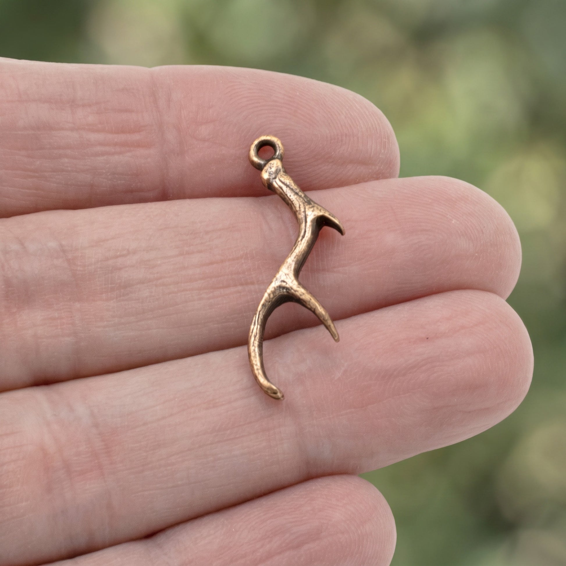 Hackberry Creek antique copper plated pewter antler charm held between fingers for jewelry making