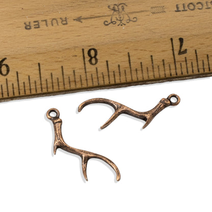 Hackberry Creek pair of antique copper plated pewter antler charms for jewelry making next to a wooden ruler