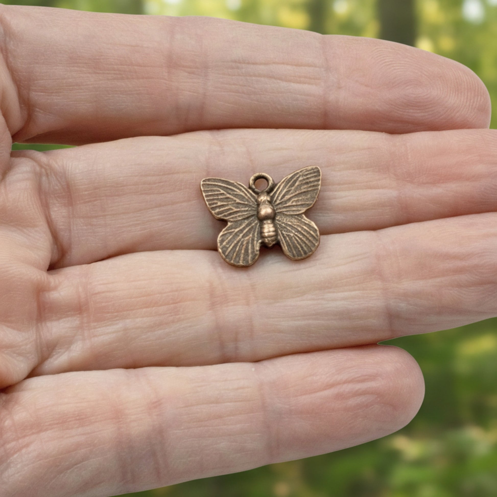 Hackberry Creek antique copper butterfly charm held in a palm, featuring detailed wings and rustic oxidized finish.