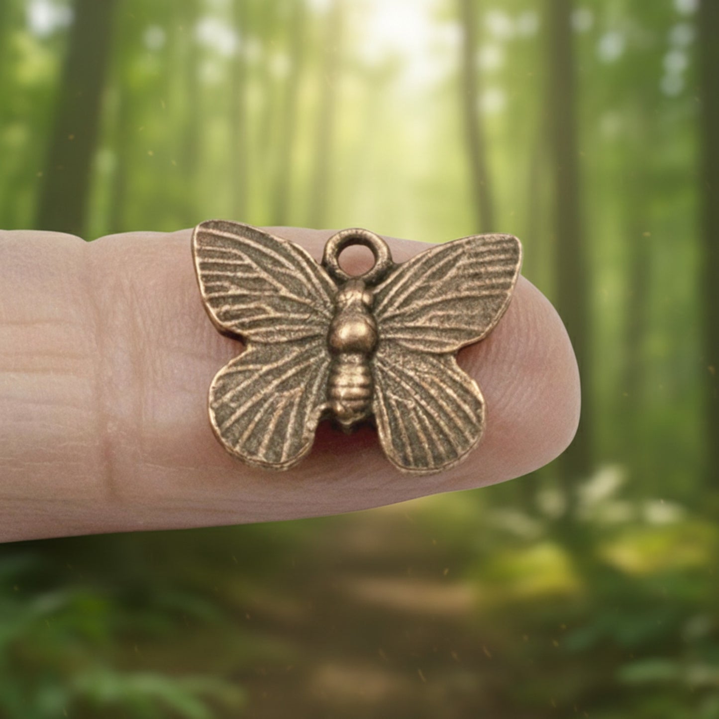 Hackberry Creek antique copper butterfly charm with detailed wing texture held on a finger against a forest background.