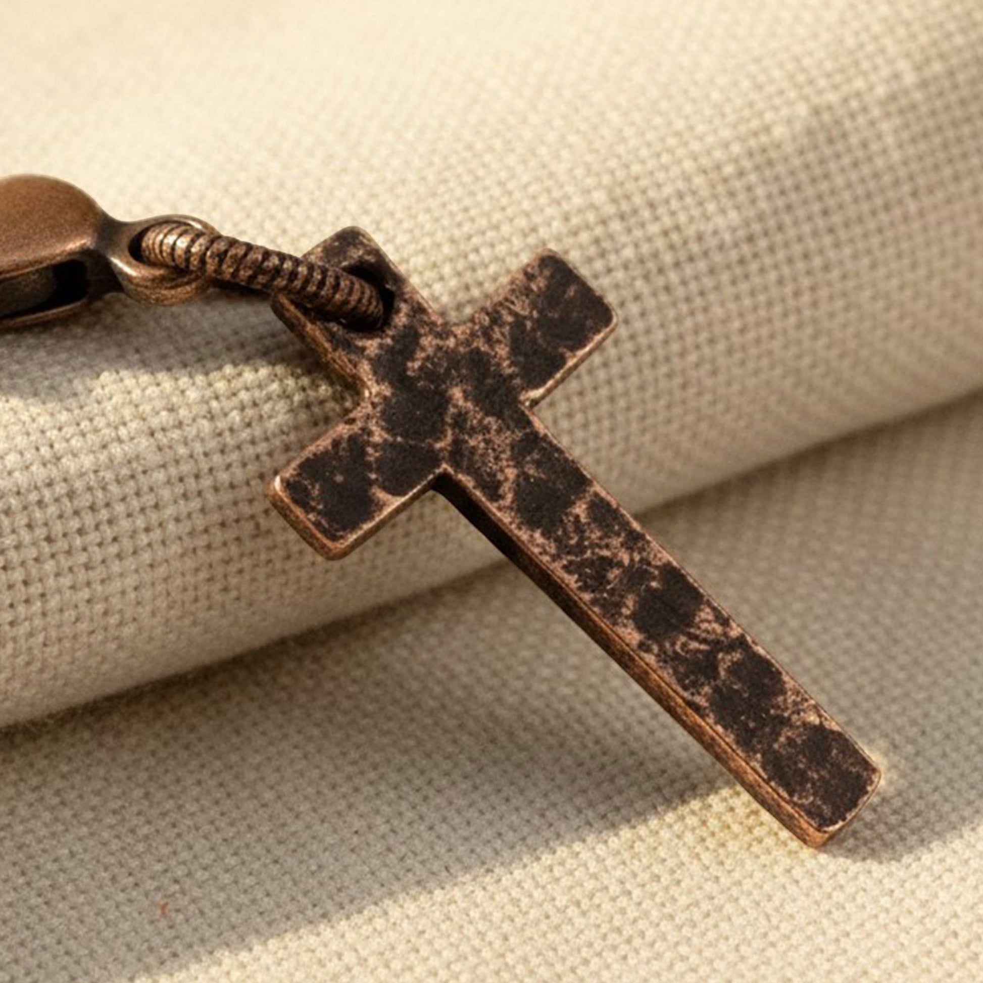 Hackberry Creek copper cross charm with distressed finish and lobster clasp on textured cream fabric background.