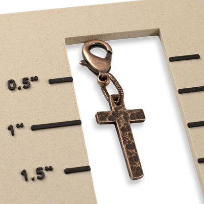 Hackberry Creek copper cross clip-on charm with a distressed finish and lobster clasp on a measurement scale.