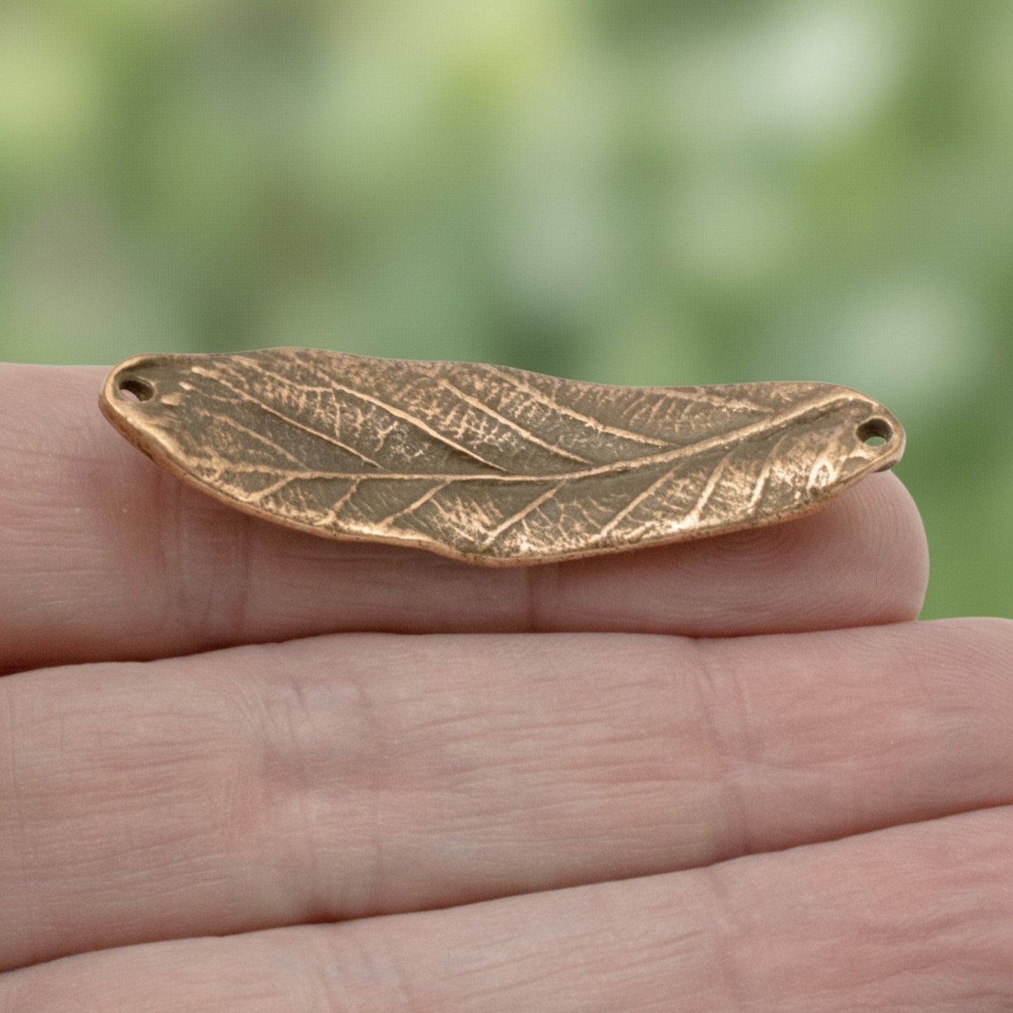 Hackberry Creek antique copper leaf bracelet connector link with organic textured detail held in a hand.