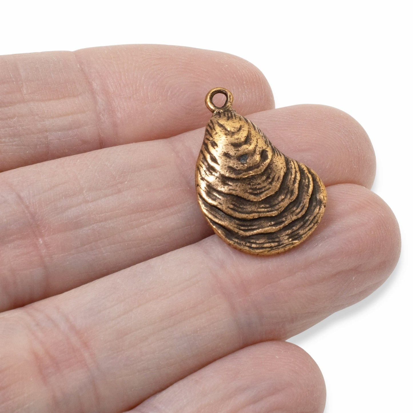 Hackberry Creek antique copper oyster shell charm held in hand, featuring detailed ridges and coastal design.
