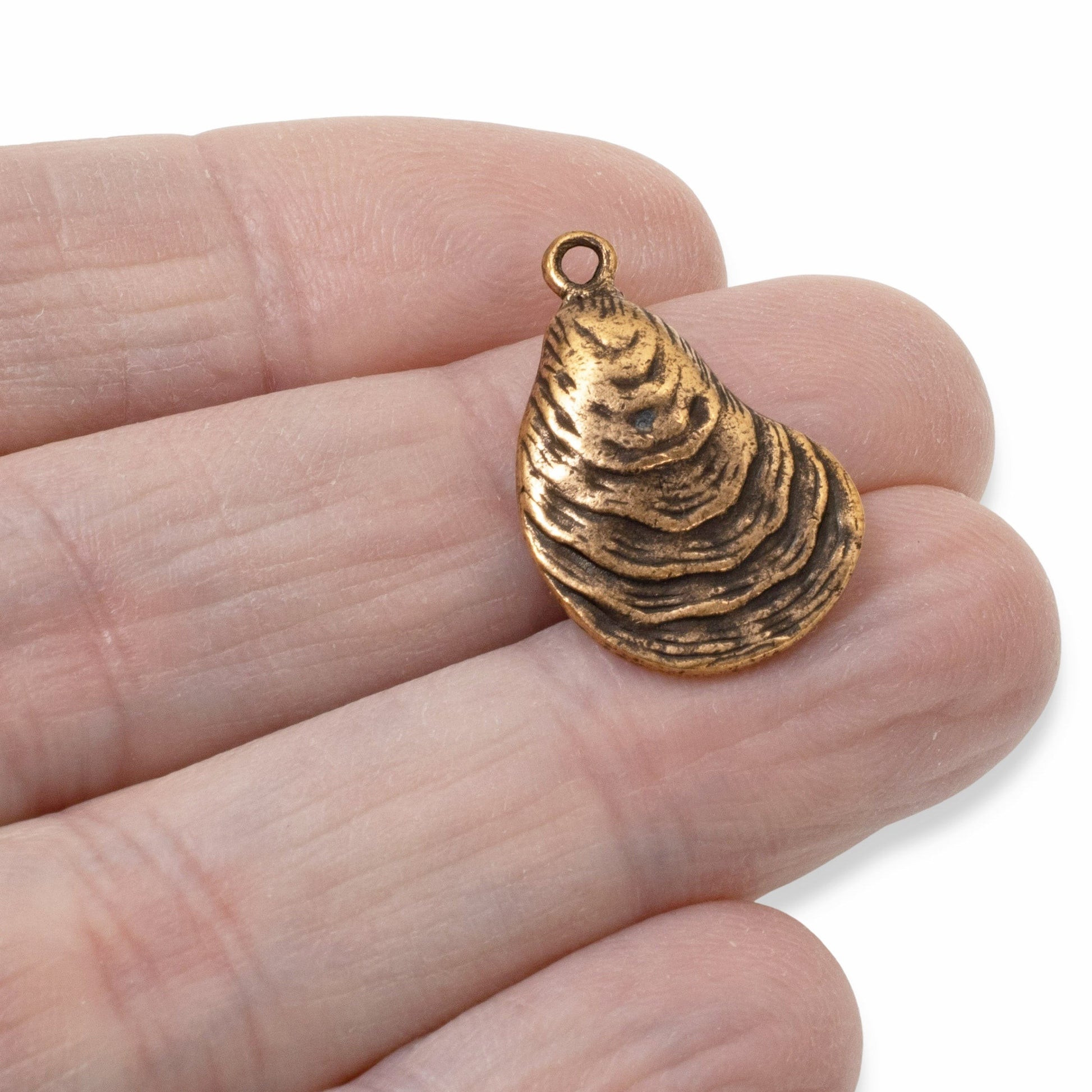 Hackberry Creek antique copper oyster shell charm held in hand, featuring detailed ridges and coastal design.