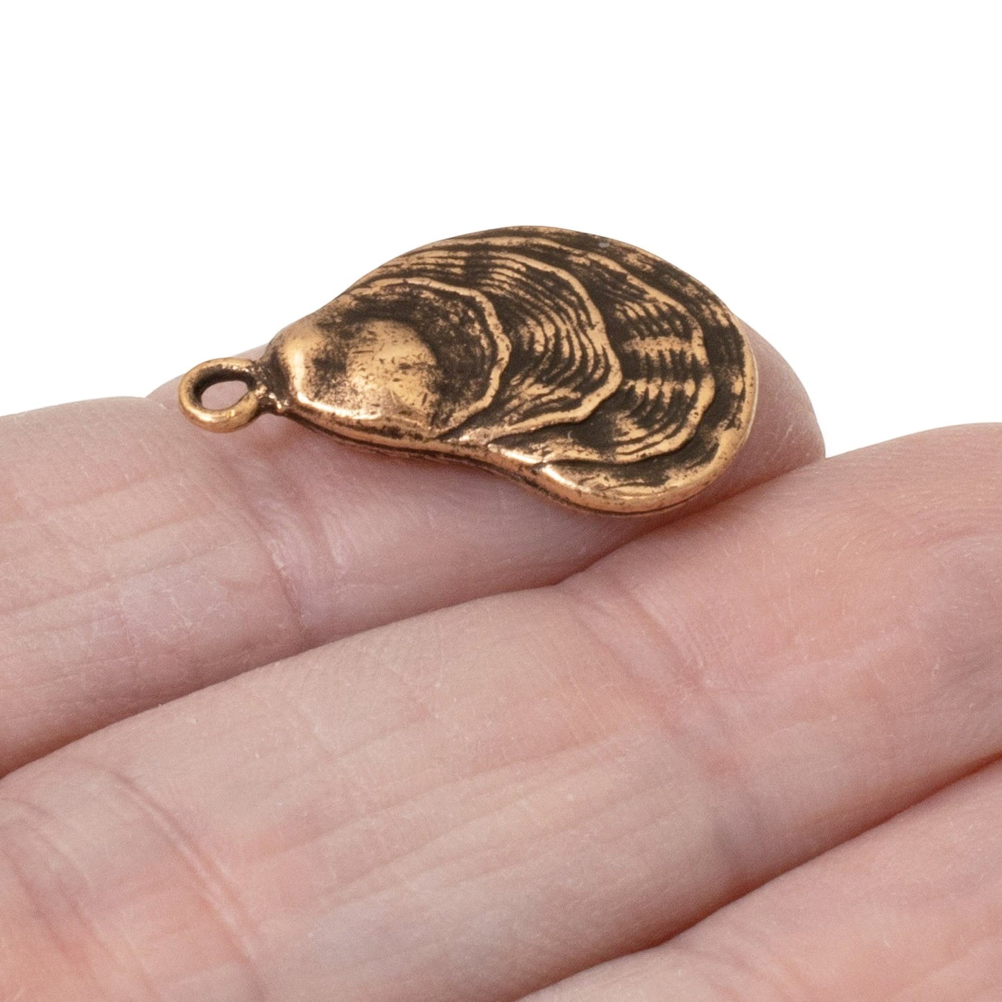 Hackberry Creek antique copper oyster shell charm held on a finger, showing detailed coastal texture.