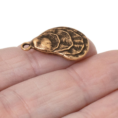 Hackberry Creek antique copper oyster shell charm held on a finger, showing detailed coastal texture.