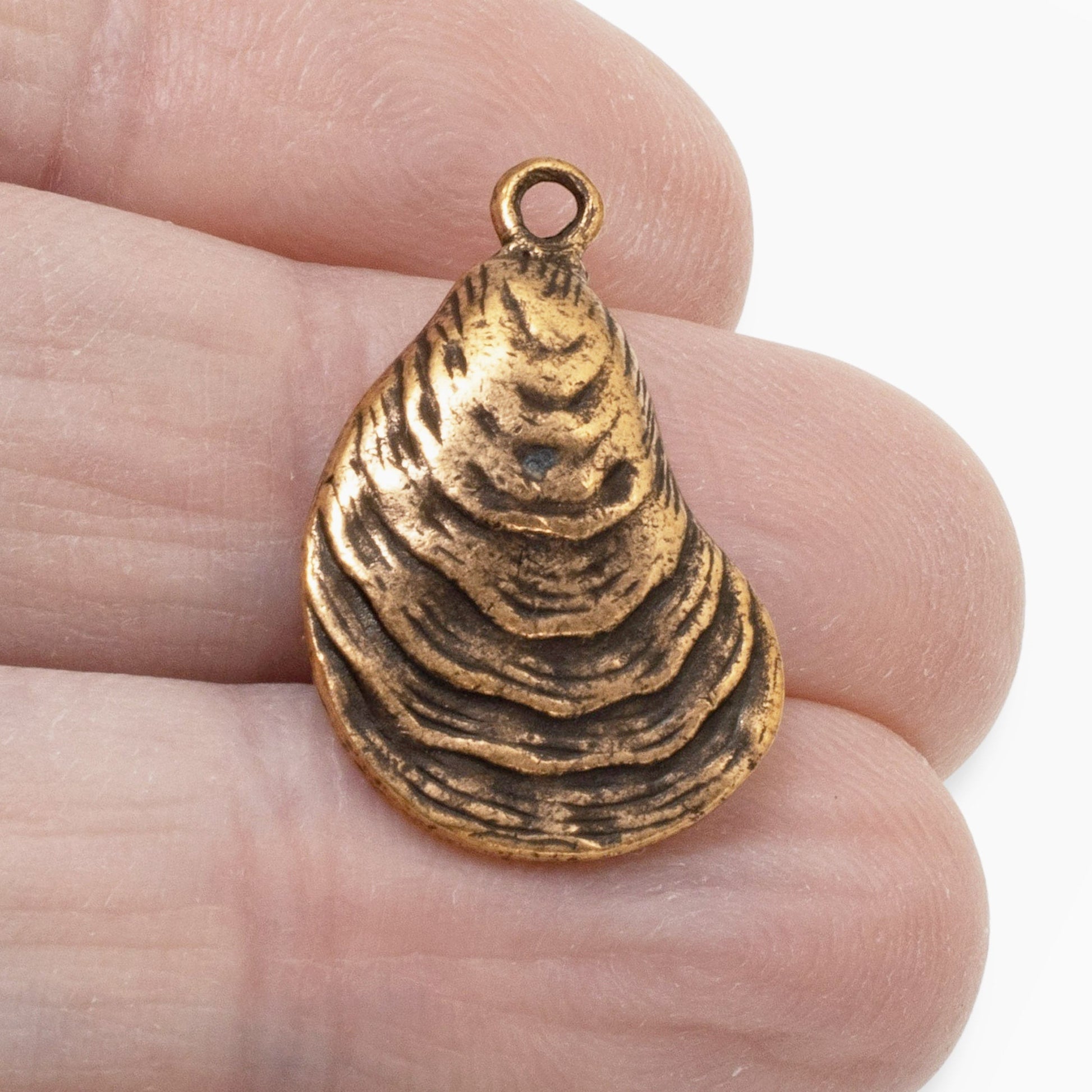 Hackberry Creek antique copper oyster shell charm held between fingers, showing detailed coastal texture.
