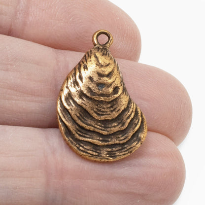 Hackberry Creek antique copper oyster shell charm held between fingers, showing detailed coastal texture.