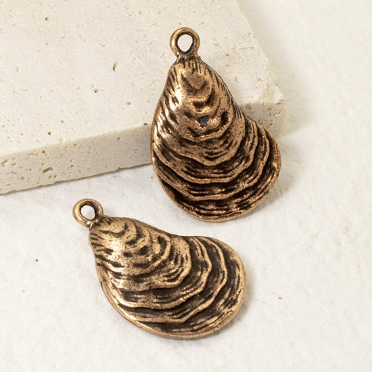 Hackberry Creek antique copper oyster shell charms with detailed ridges, perfect for coastal jewelry designs.