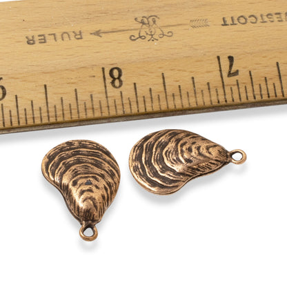 Hackberry Creek antique copper oyster shell charms with detailed texture, shown next to a ruler for scale.