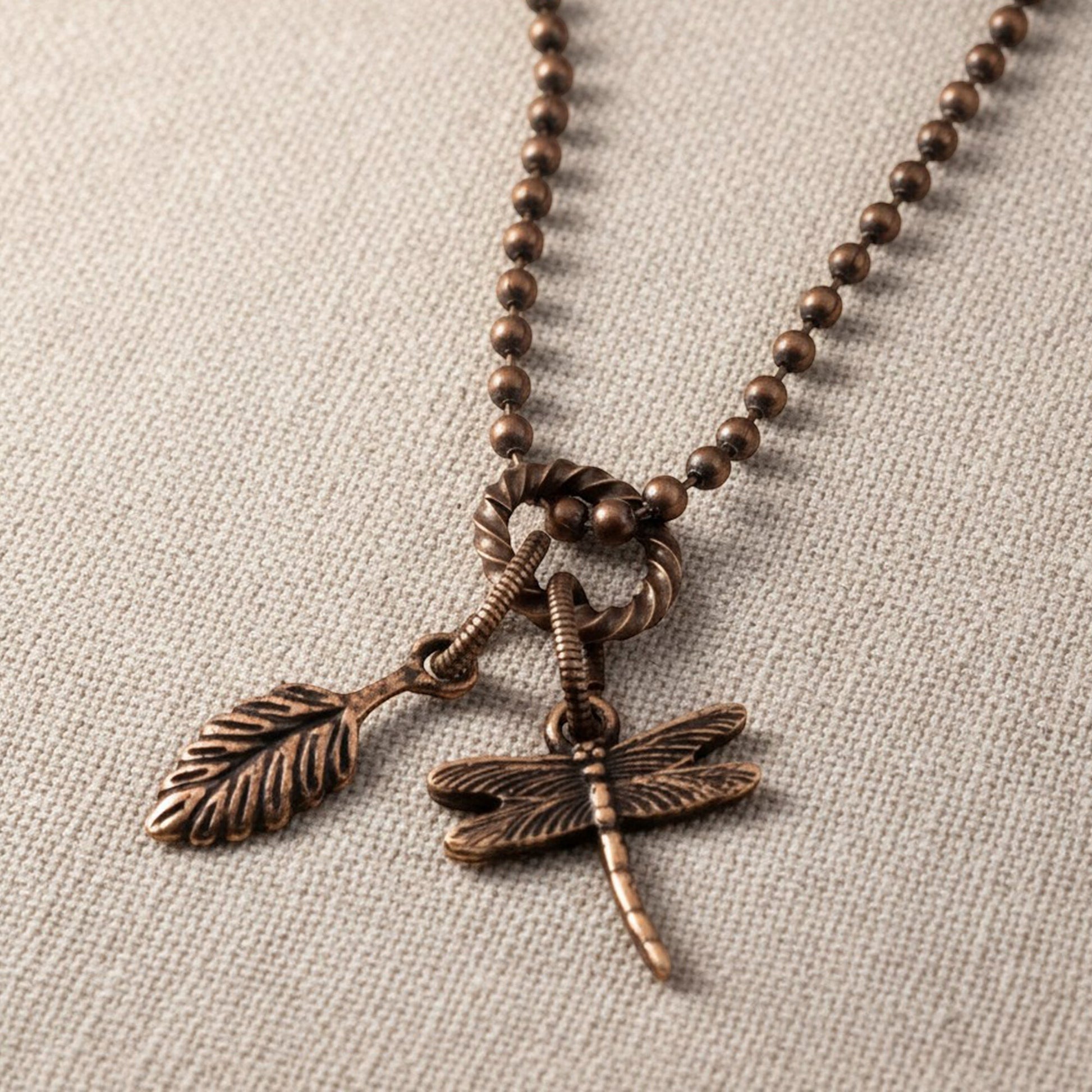 Hackberry Creek antique copper rope jump ring connecting a leaf charm and a dragonfly charm on a beaded chain.