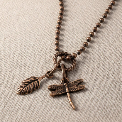 Hackberry Creek antique copper rope jump ring connecting a leaf charm and a dragonfly charm on a beaded chain.