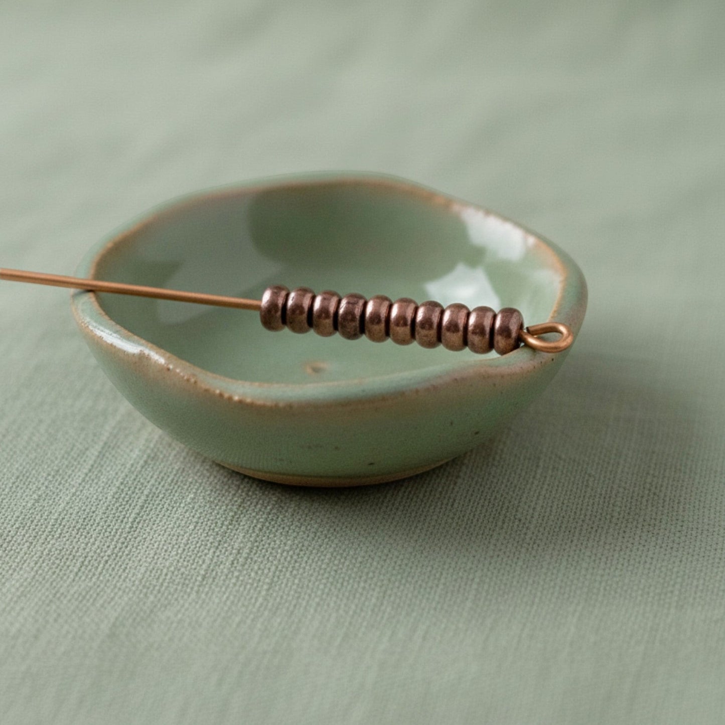 Hackberry Creek 50 antique copper 3mm smooth heishi spacer beads on a wire in a light green dish.