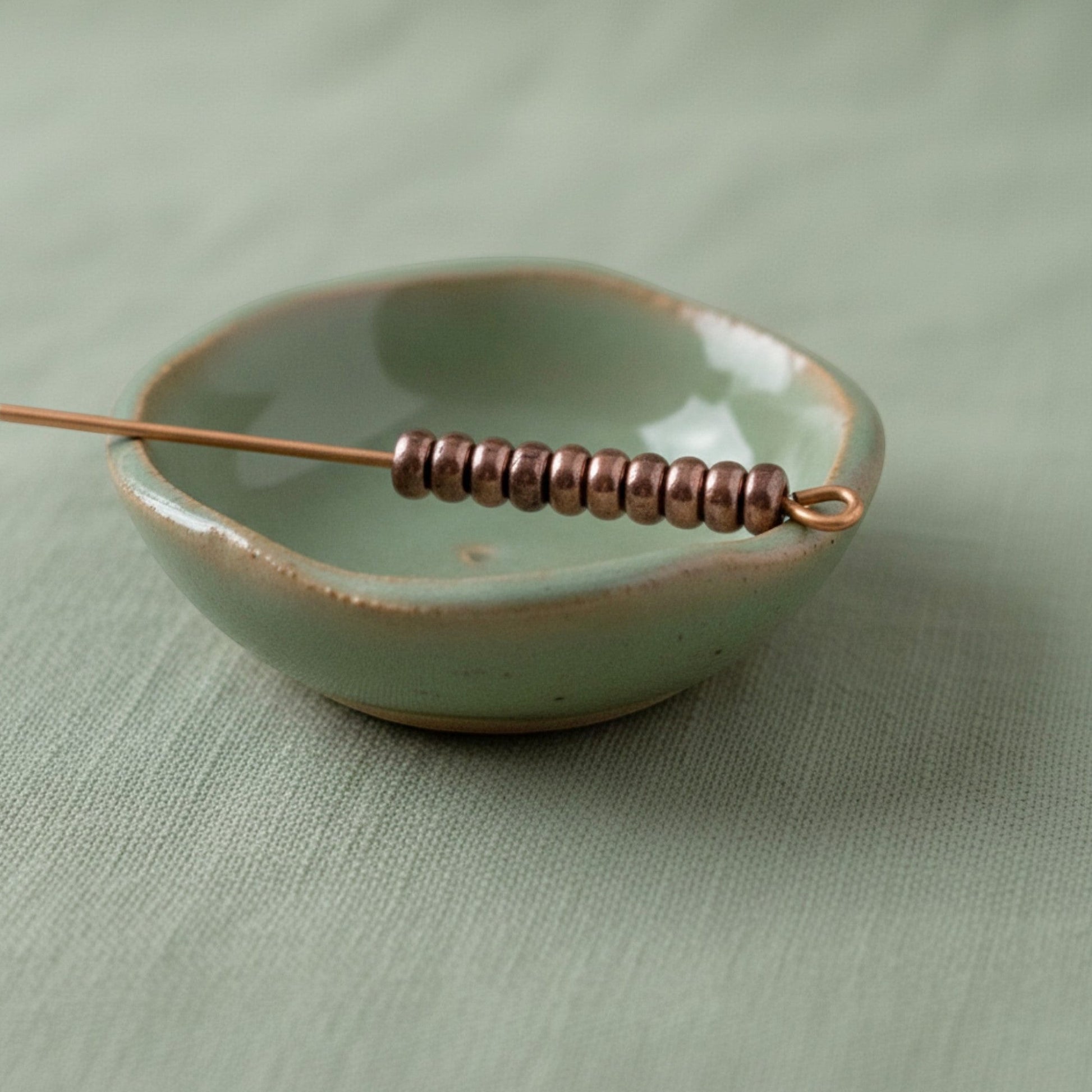 Hackberry Creek 50 antique copper 3mm smooth heishi spacer beads on a wire in a light green dish.