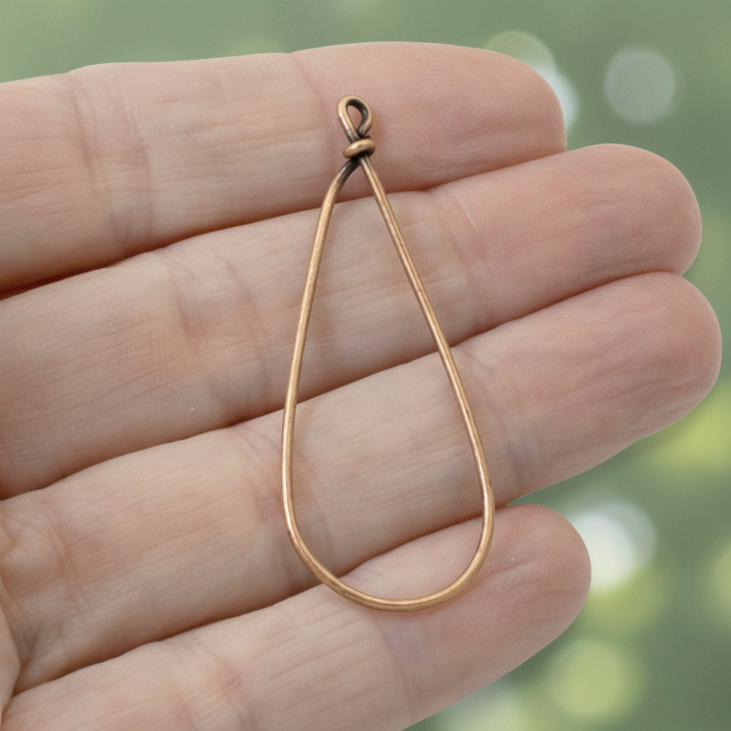 Hackberry Creek large teardrop earring frame in antique copper finish held in a hand for jewelry making.