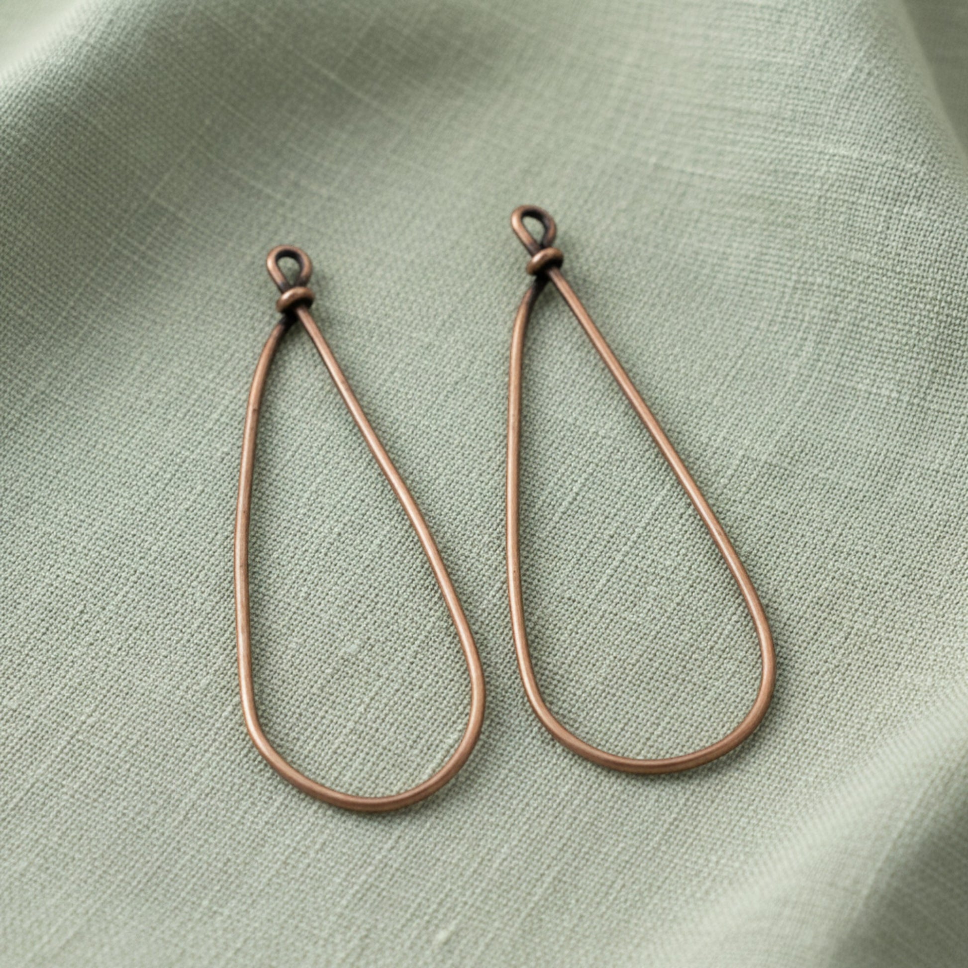 Hackberry Creek large copper teardrop earring frames for DIY jewelry making on a sage green linen background.