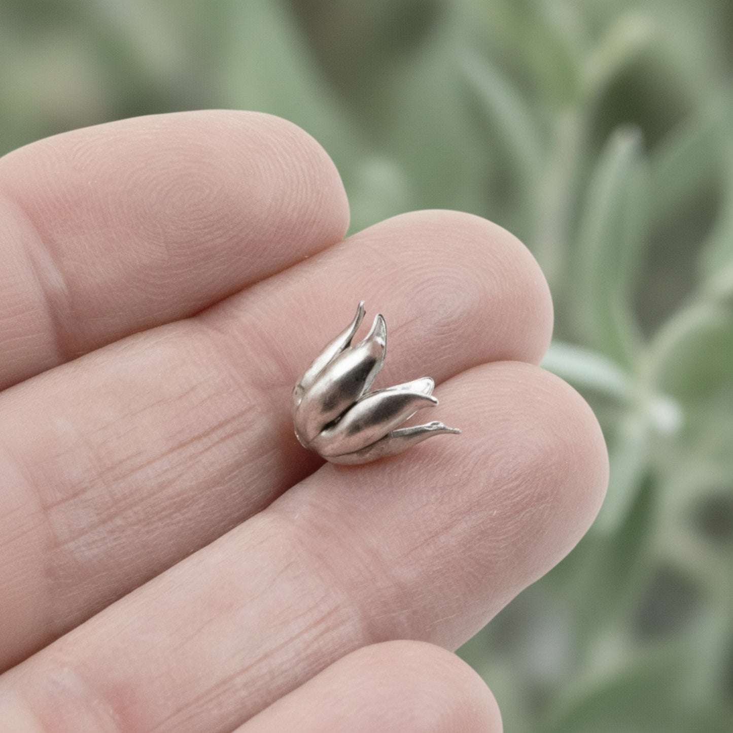 Hackberry Creek antique silver-plated pewter curled petal bead cap held between fingers for scale