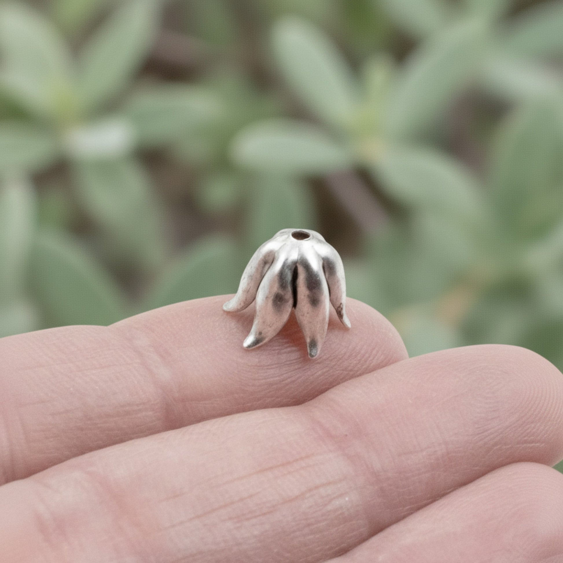 Hackberry Creek curled petal bead cap in antique silver-plated pewter held on a finger for scale