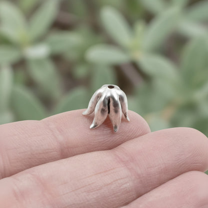 Hackberry Creek curled petal bead cap in antique silver-plated pewter held on a finger for scale