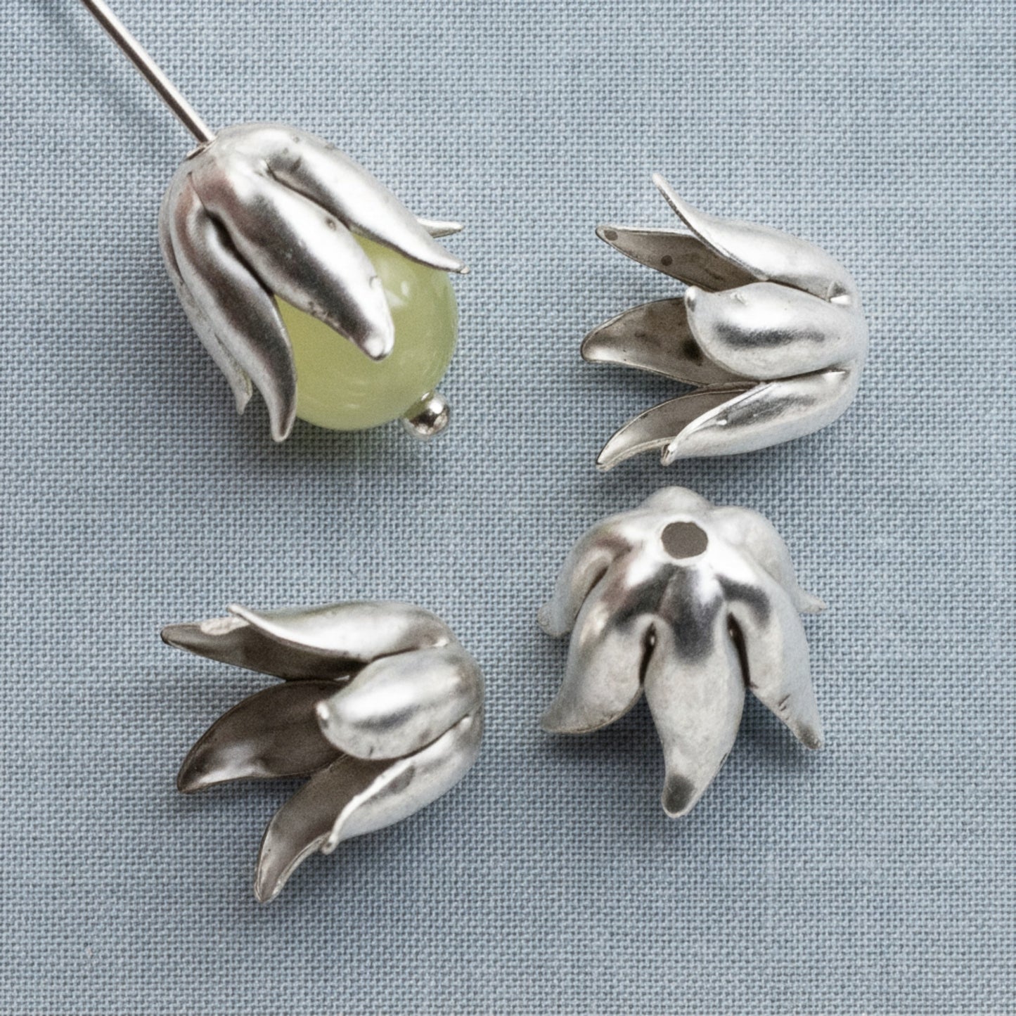 Hackberry Creek antique silver-plated pewter curled petal bead caps for 8mm beads on a blue fabric background.
