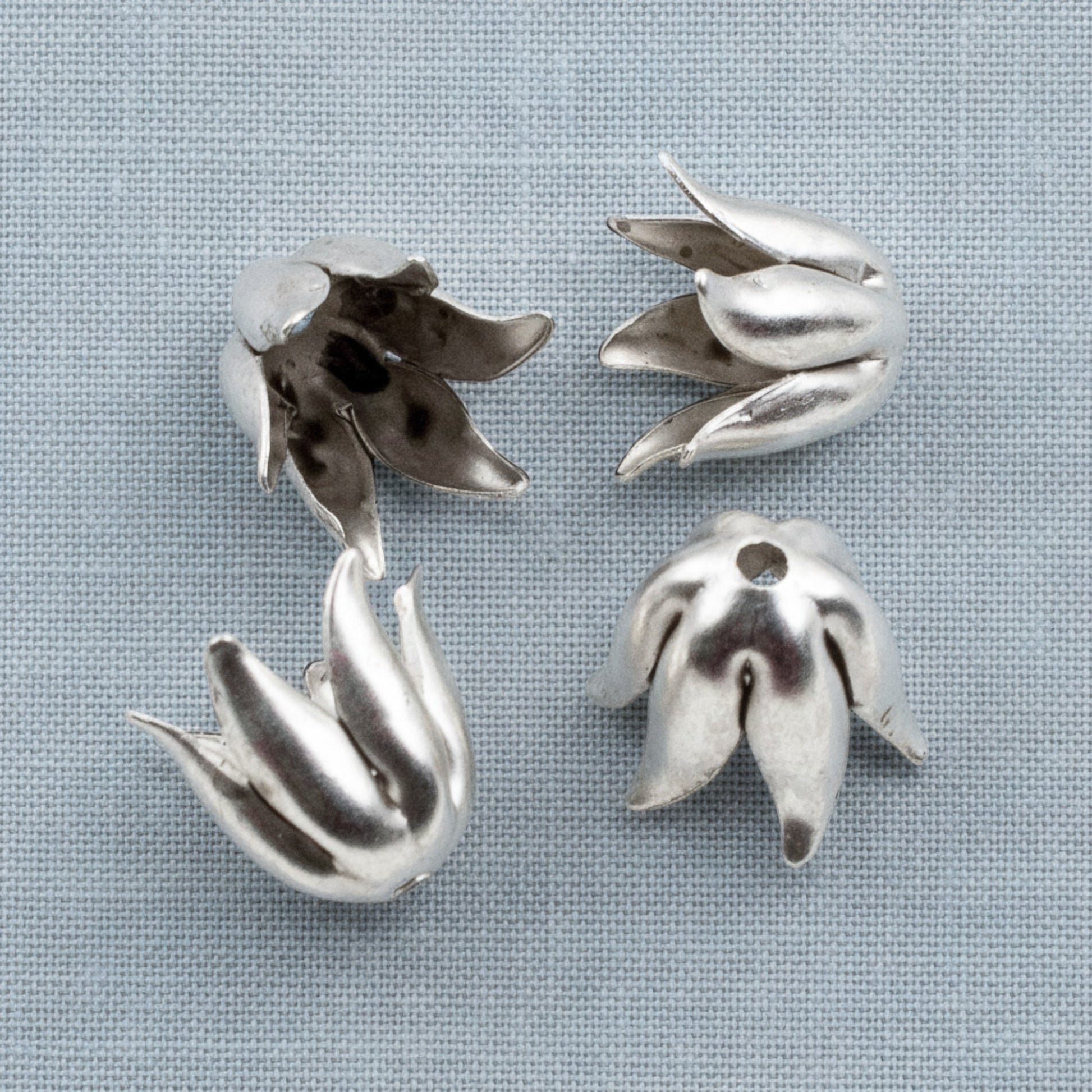 Hackberry Creek antique silver-plated pewter curled petal bead caps for 8mm jewelry beads on a grey fabric background